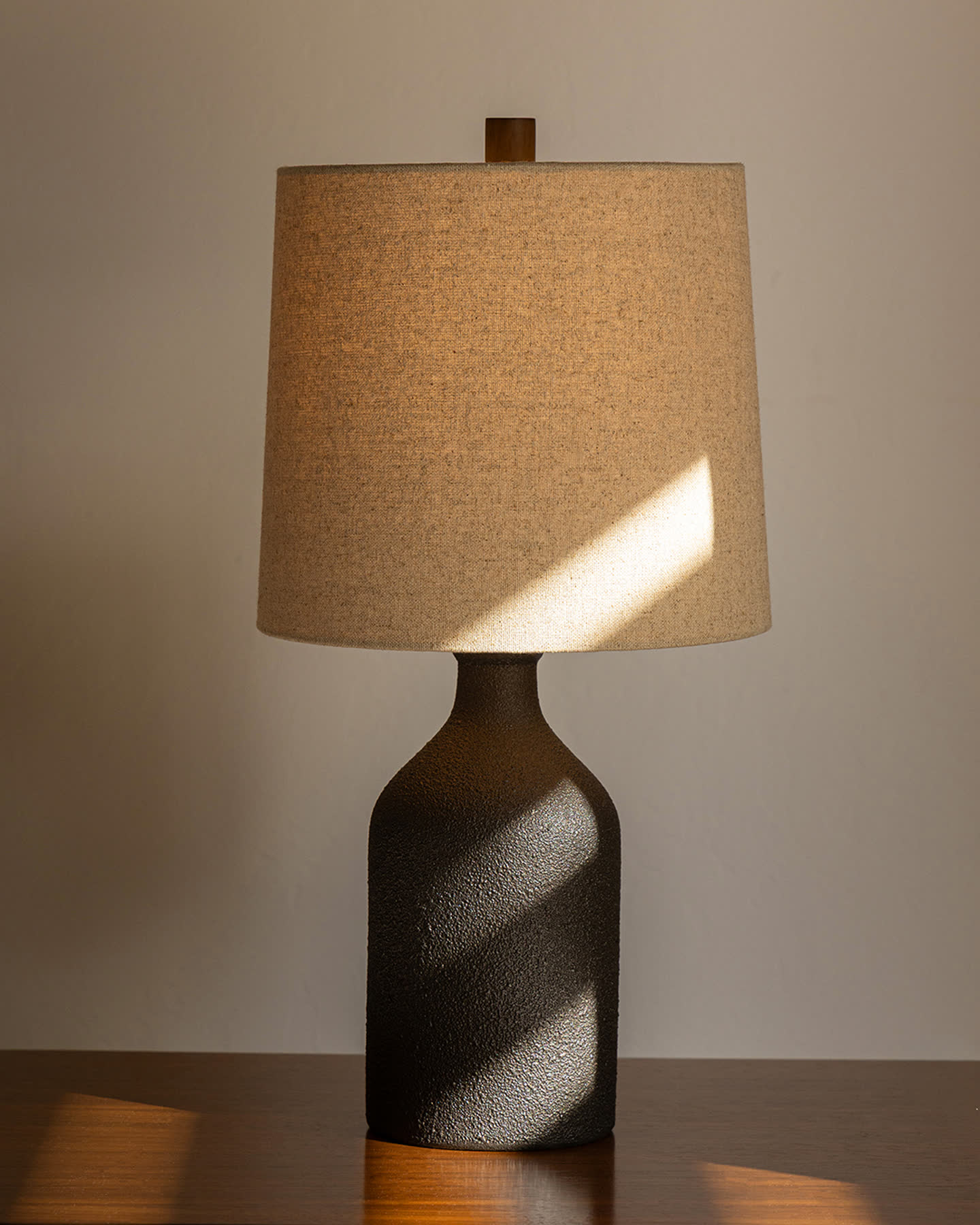 Bottle Table Lamp with a linen shade on a walnut surface, lit by angled sunlight.