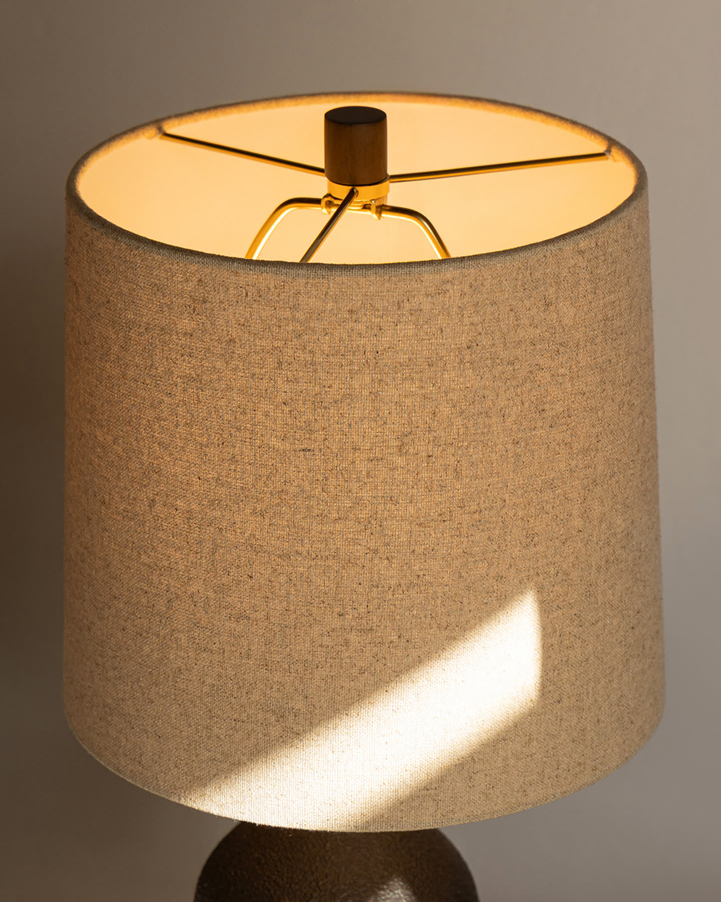 Close view of the Bottle Table Lamp&rsquo;s illuminated linen shade and bronze ceramic base.