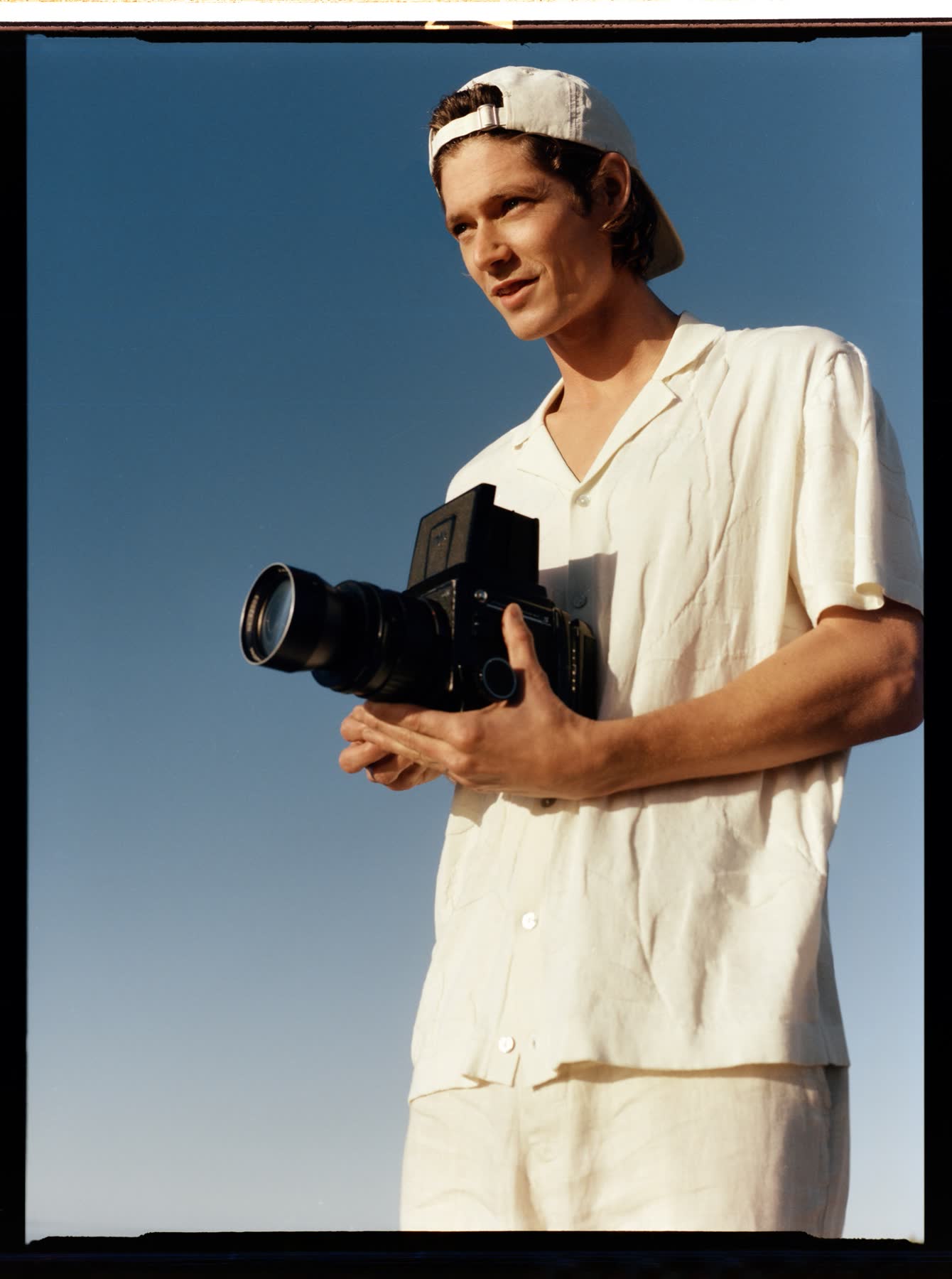 A close portrait of Conrad Leadley holding a camera against the blue sky.