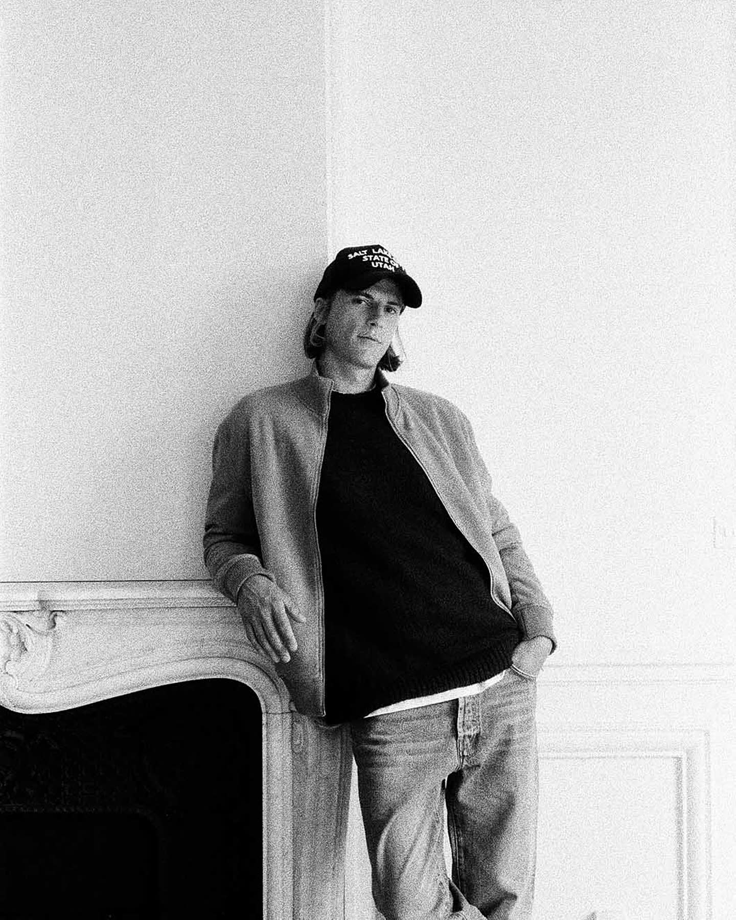 Model in a cap and cardigan beside a fireplace for Haussmann by Zara.