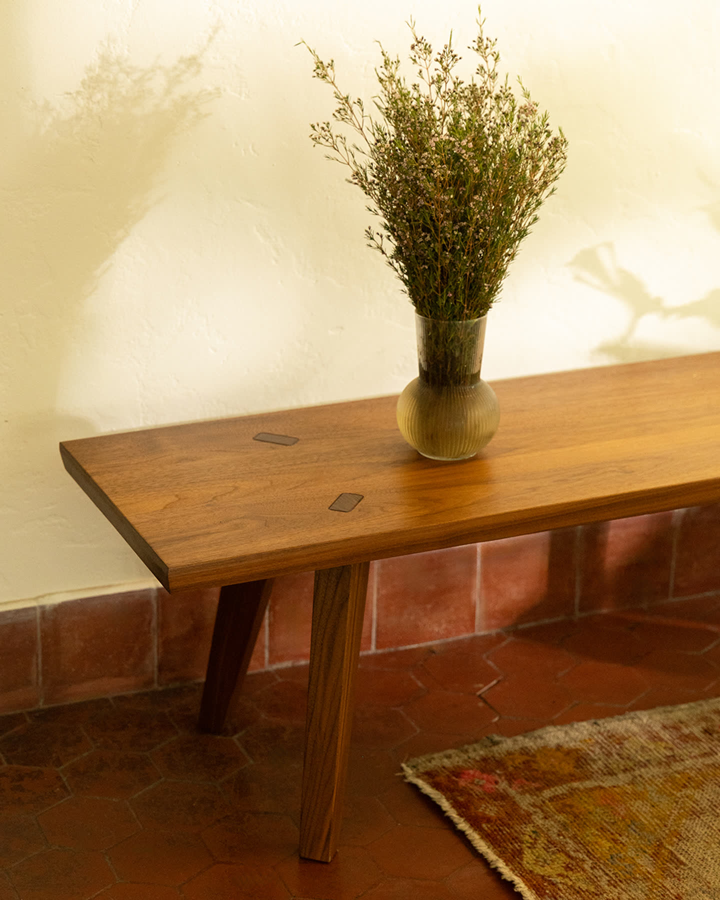 Close view of the Ojai Collection bench in walnut with a vase of branches.
