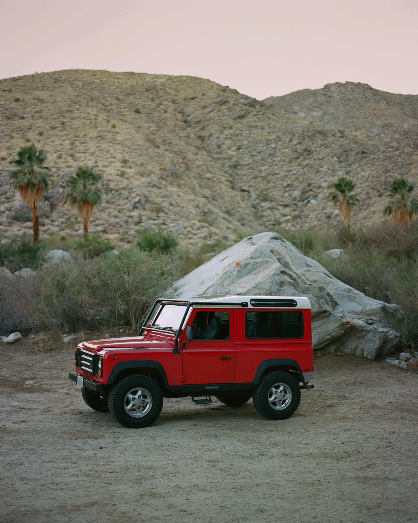 Red vehicle parked among desert boulders at sunset for Palm Springs by Zara.