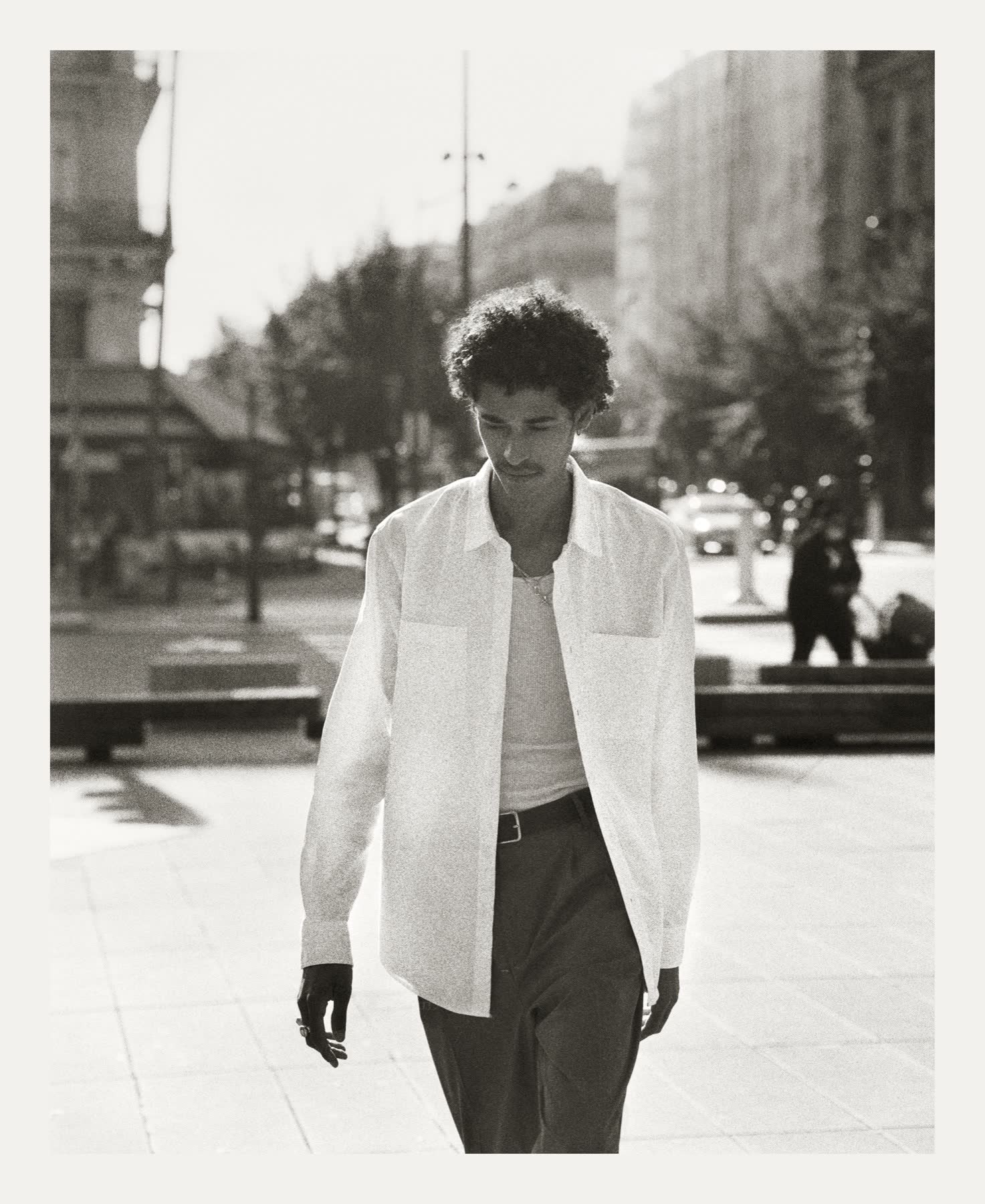 A skater walking through a Paris square in a white shirt.