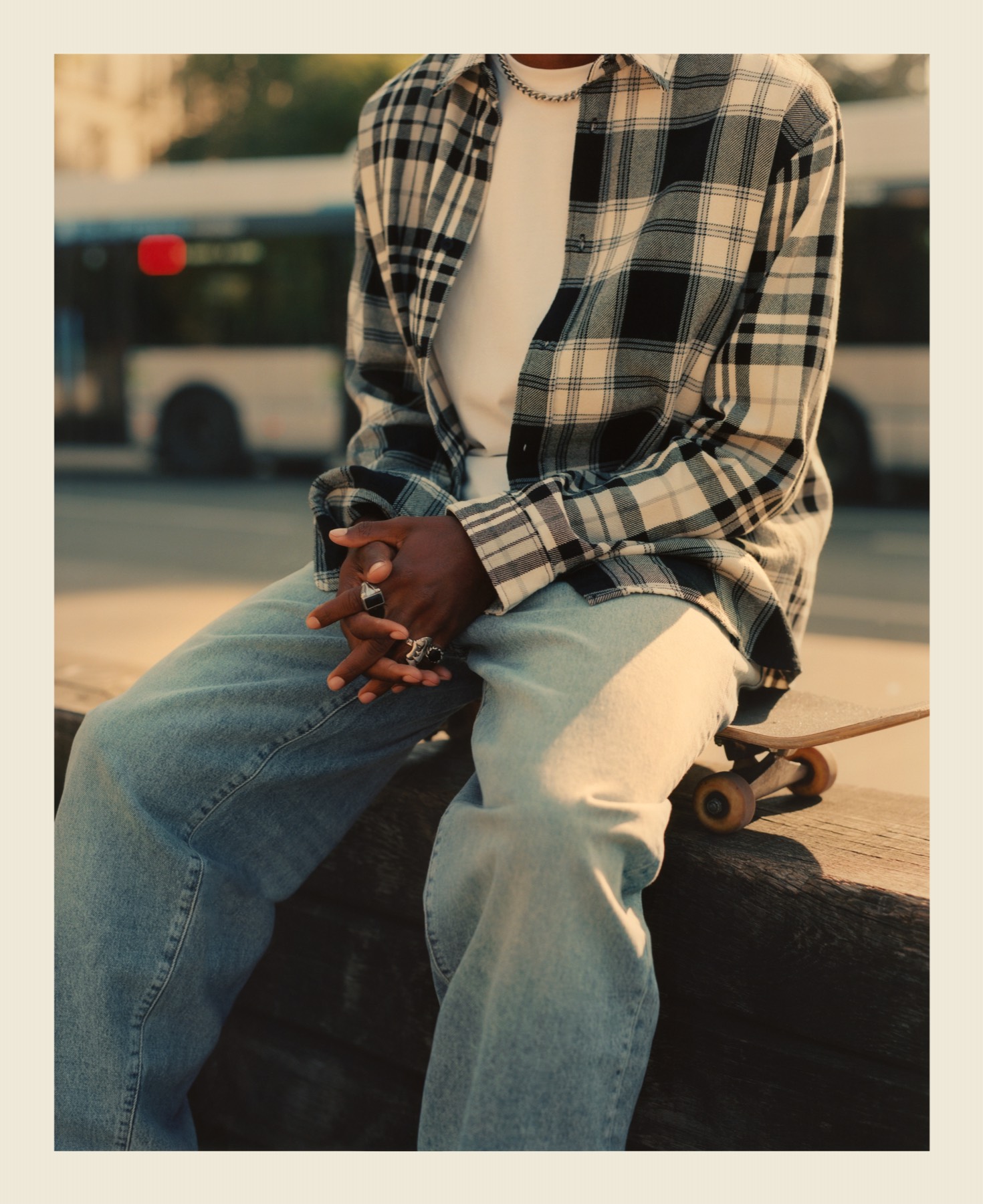 A skater in a checked shirt seated beside his board.