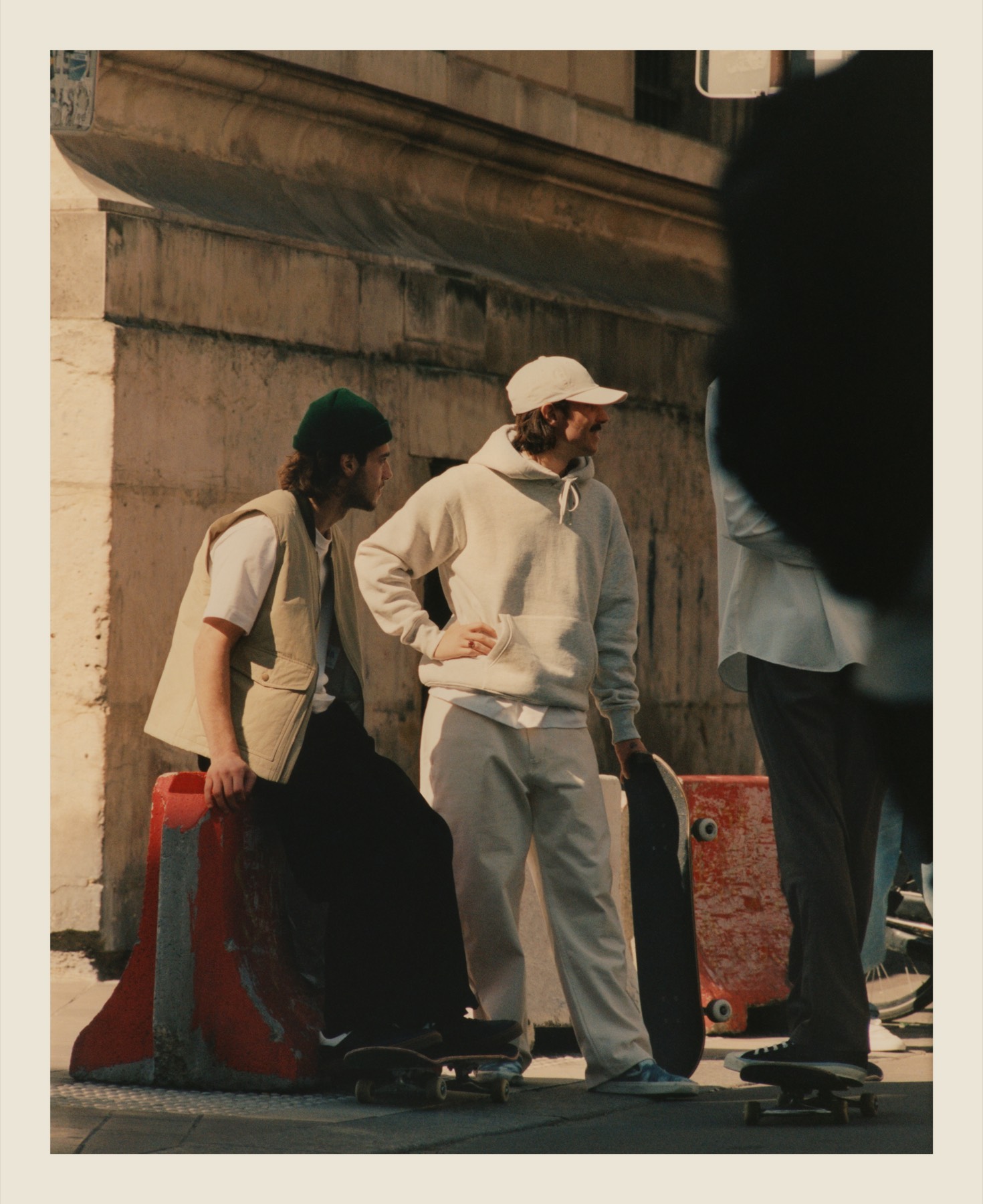 Three friends with skateboards beside a city wall.