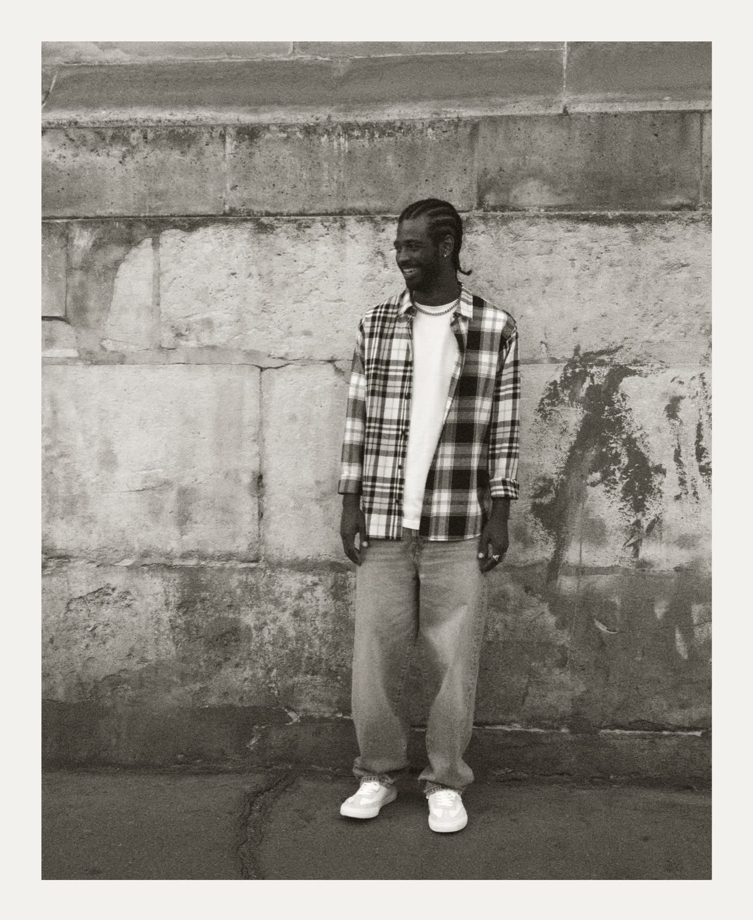A skater standing against a worn stone wall.