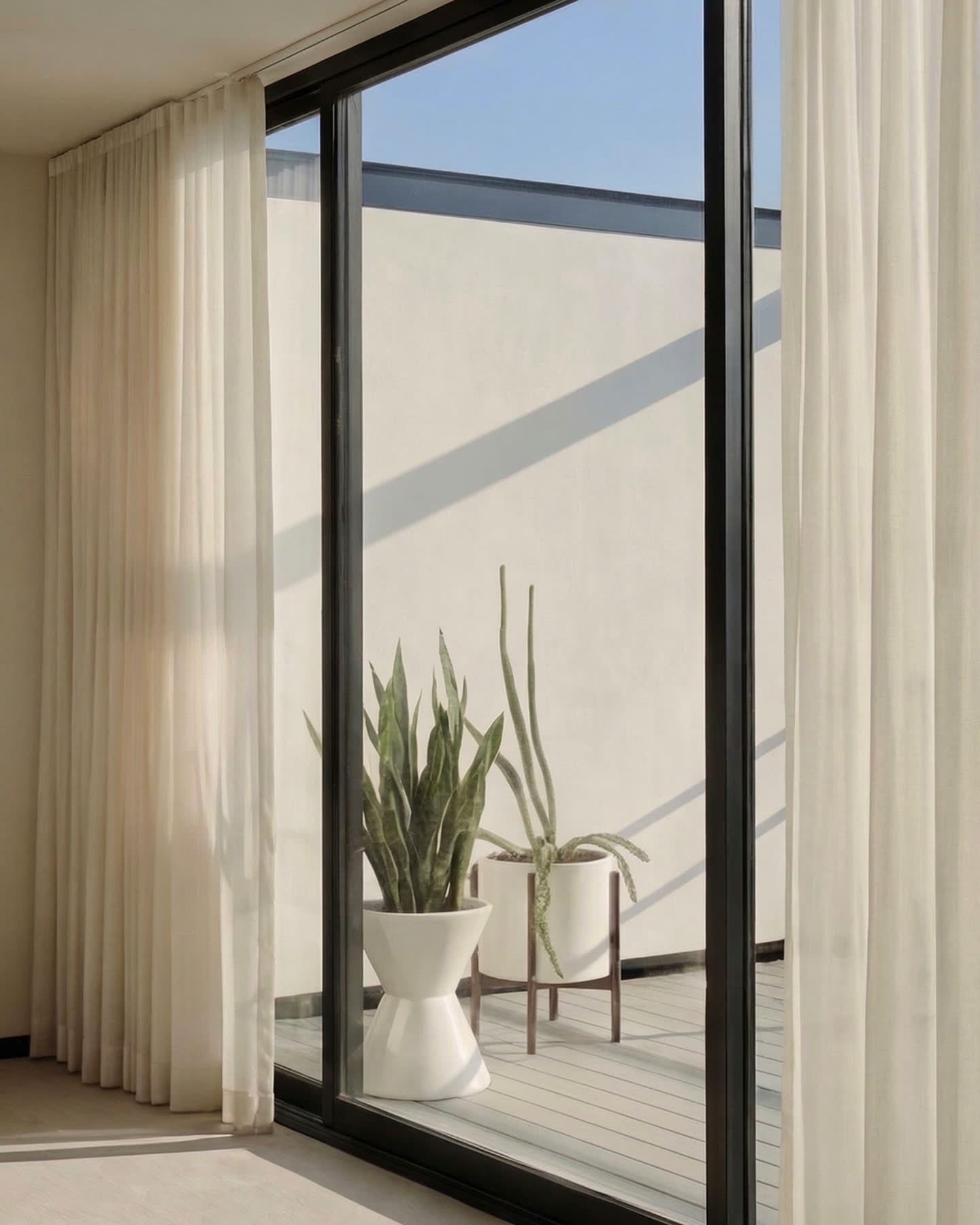 Glazed white stoneware planters framed by sheer curtains and the steel windows of the Smith House.