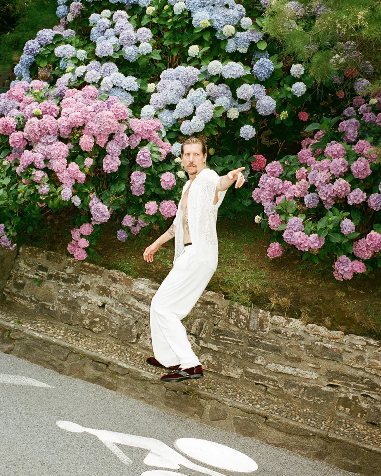 A figure in white standing before a wall of pink and blue hydrangeas.