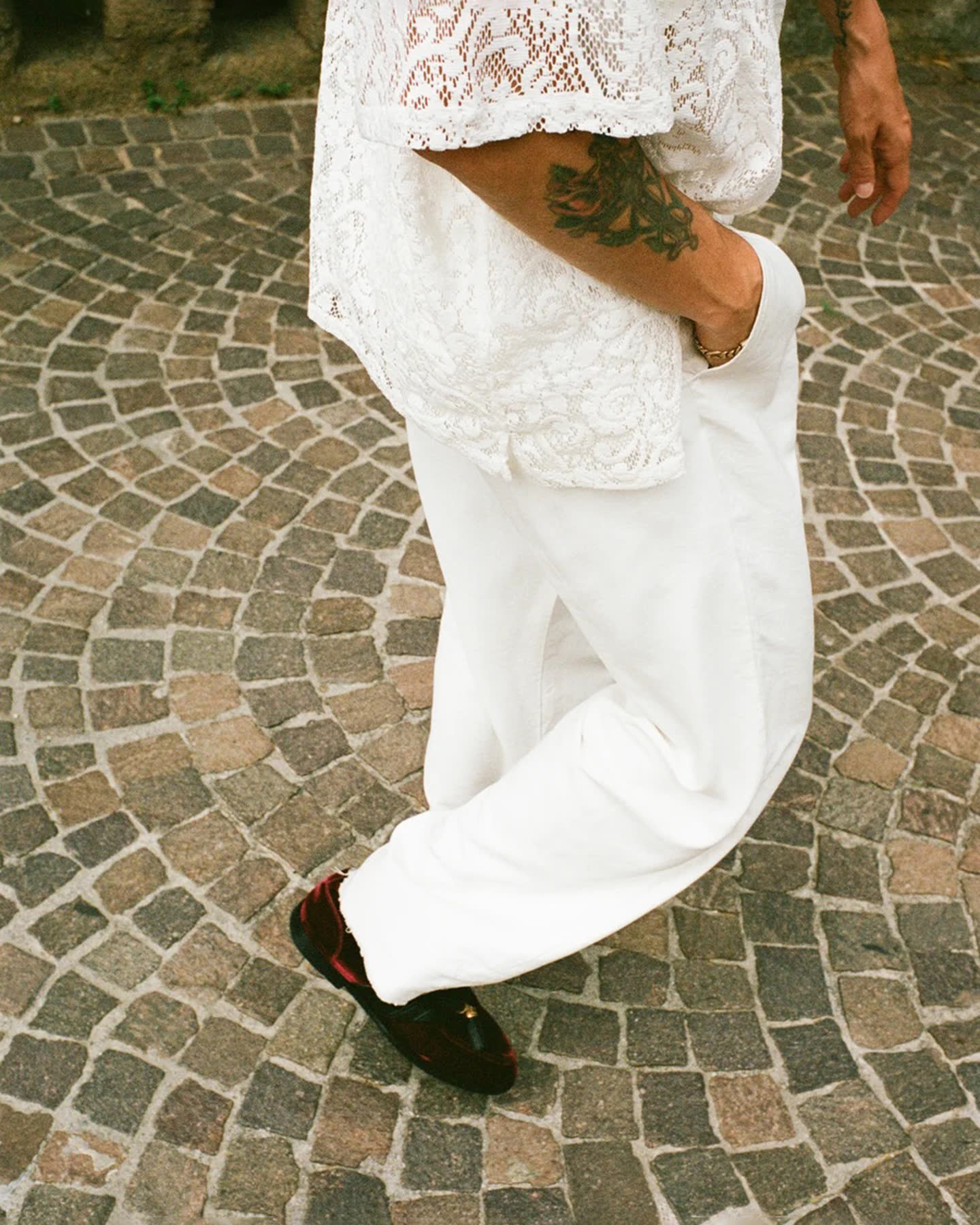 White lace clothing and burgundy loafers moving across a cobblestone street.