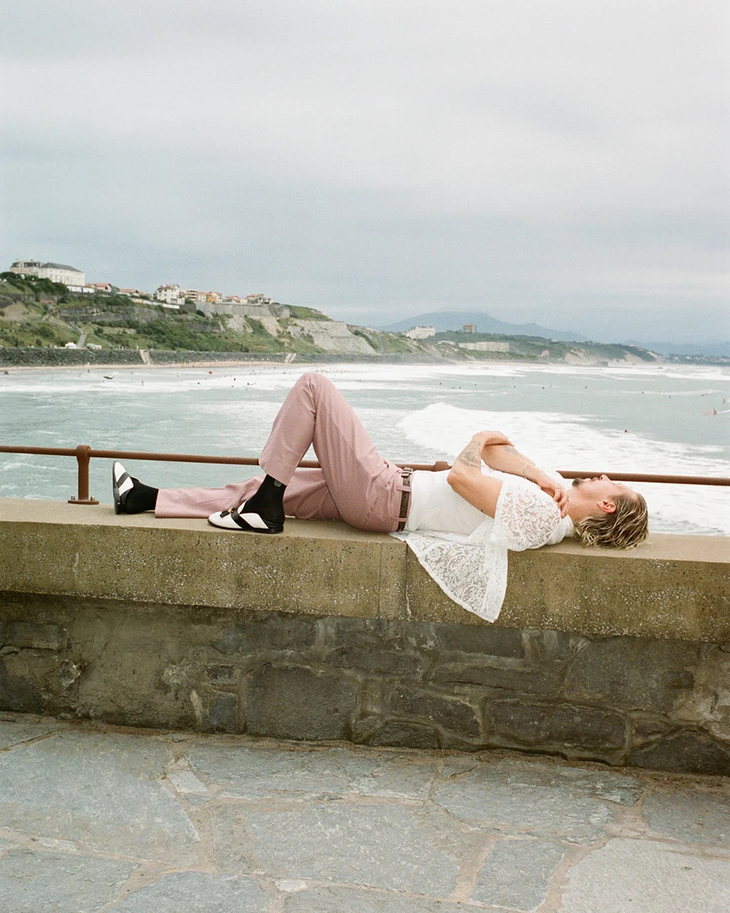 A figure reclining above the Atlantic coastline in white lace and pale pink trousers.