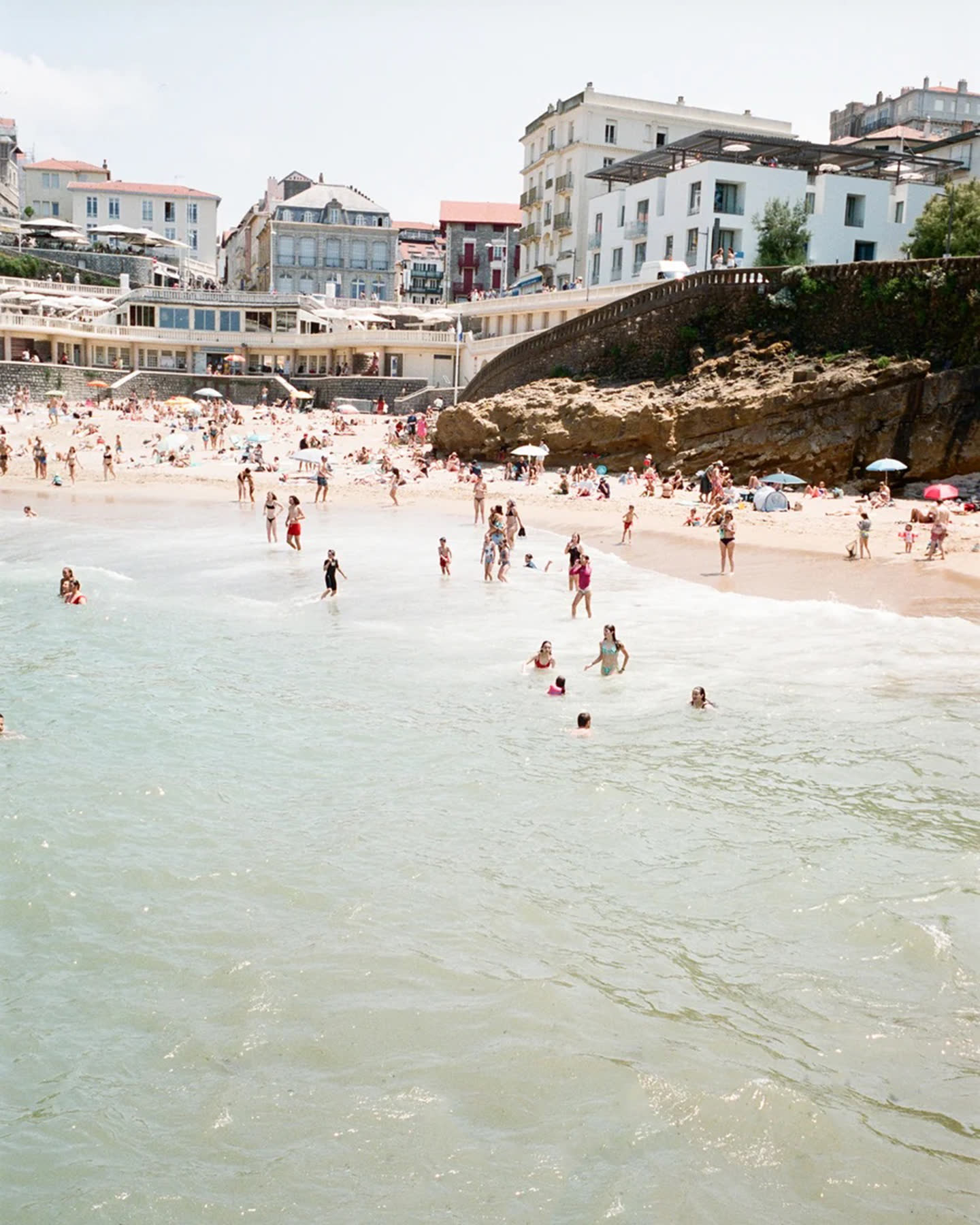 Swimmers and seaside architecture along a bright Biarritz beach.