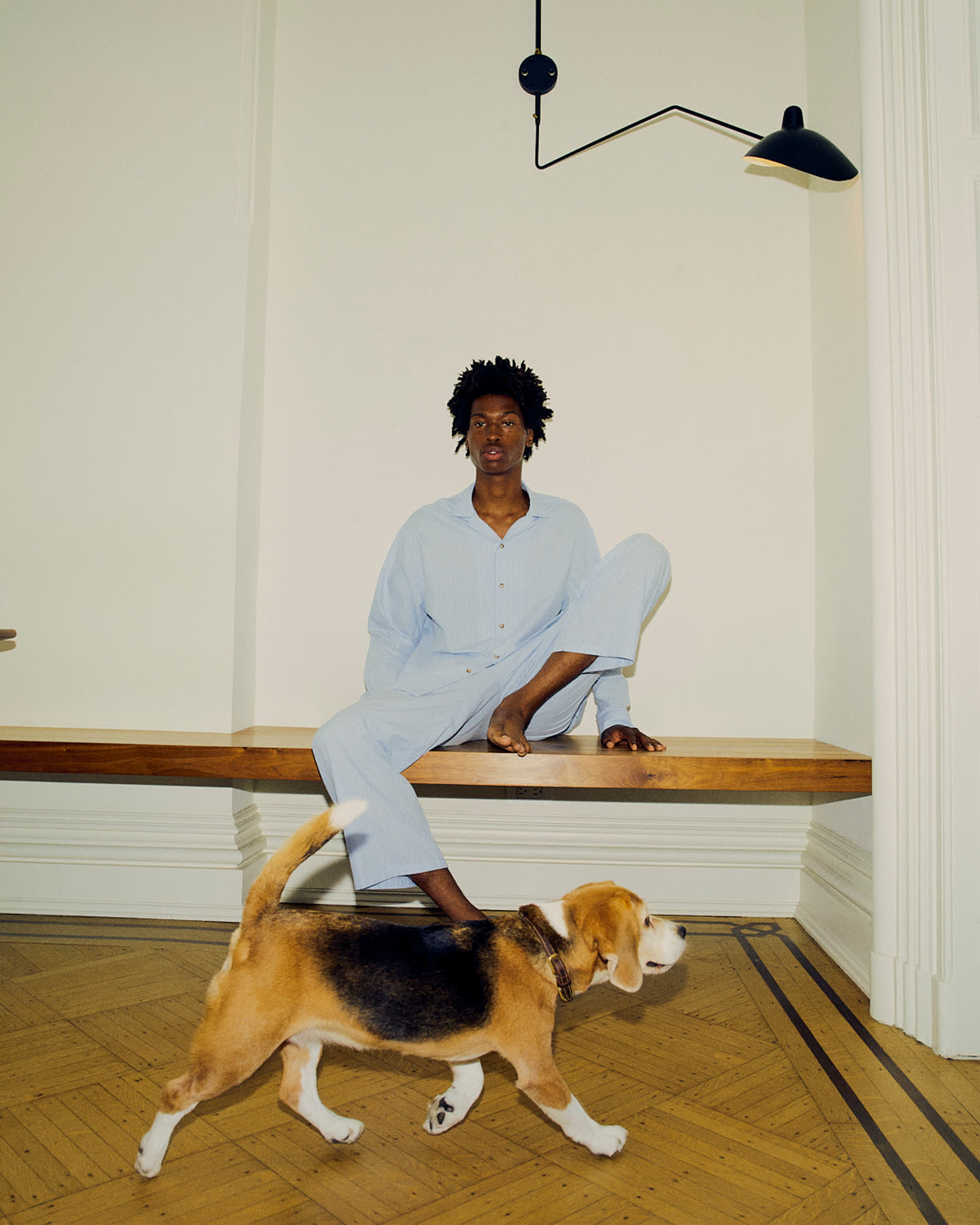 Tamel Lee seated on a wood bench as a dog crosses the room.