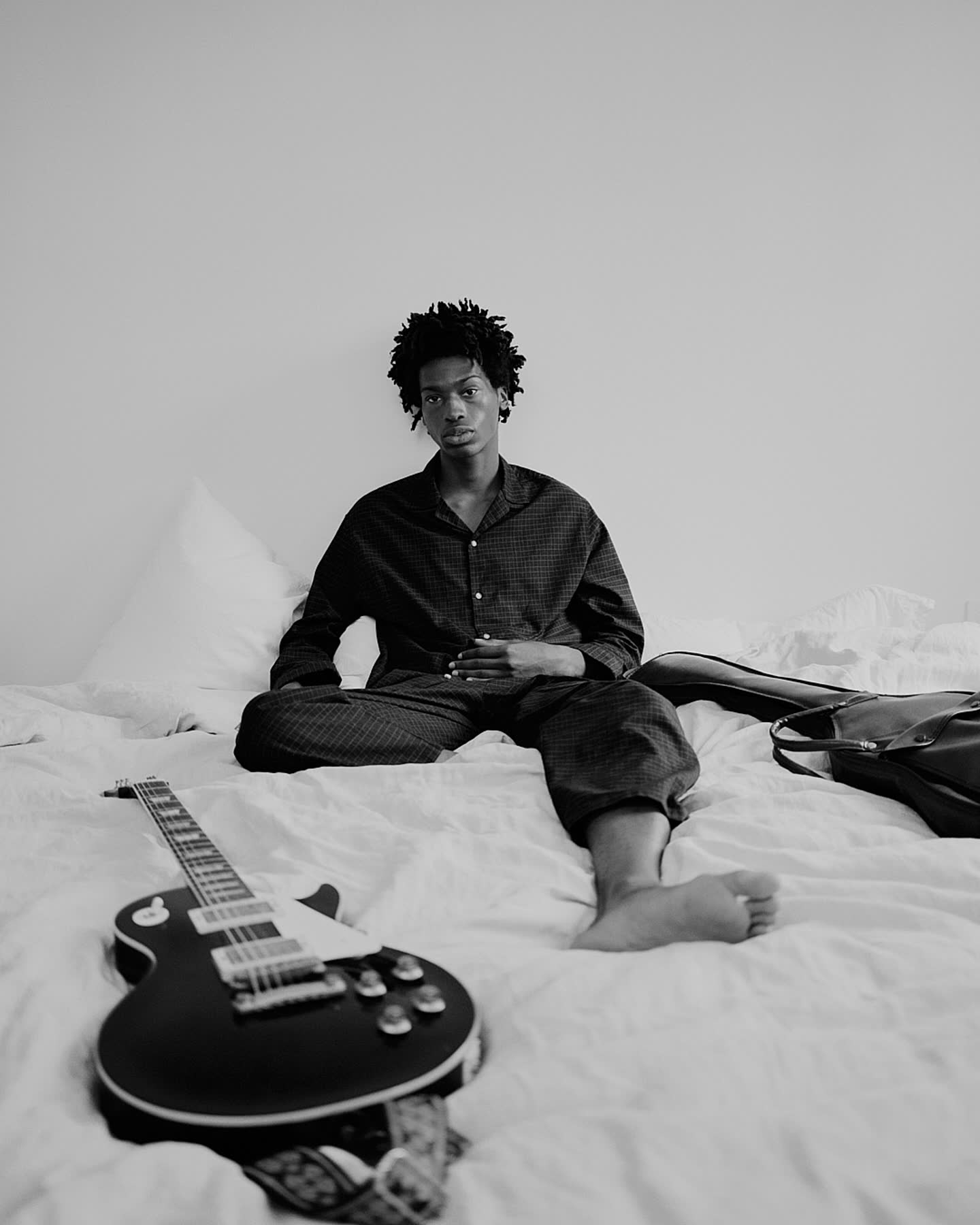 Tamel Lee seated on a bed with a guitar in black and white.