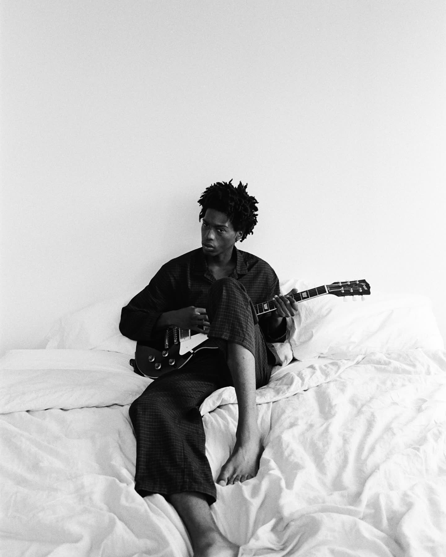 Tamel Lee playing guitar on the bed in black and white.