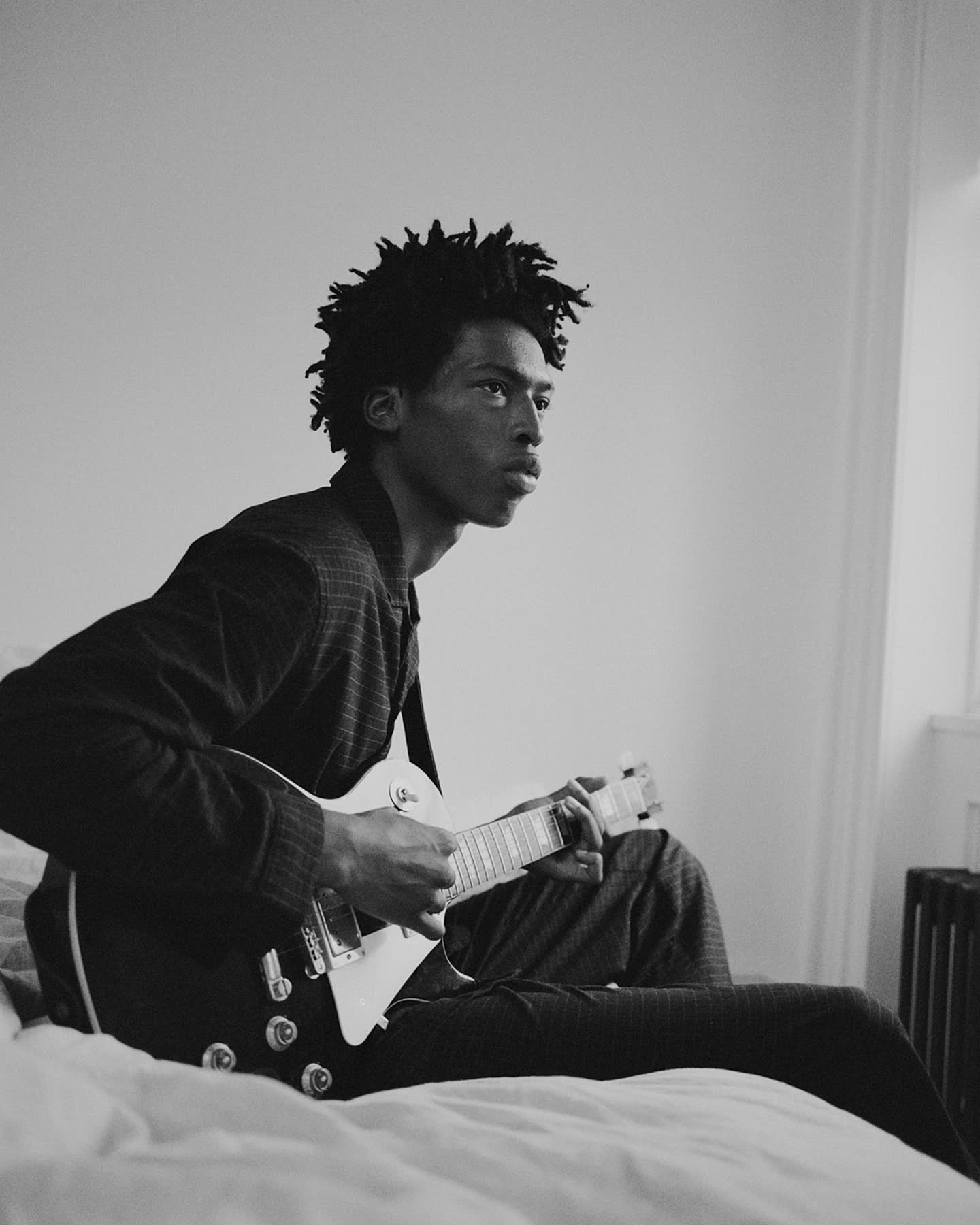 Tamel Lee playing guitar while seated on the bed.