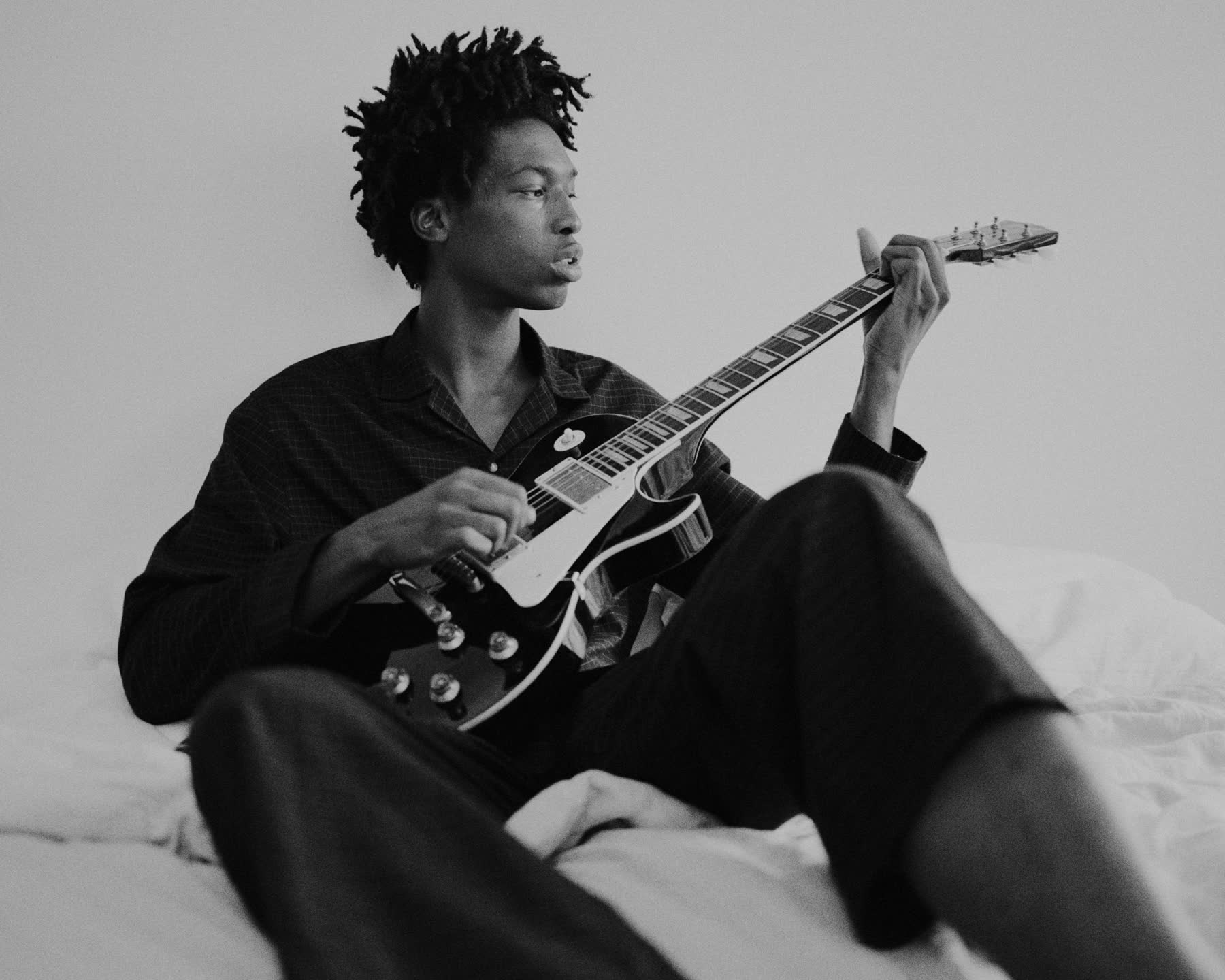 Tamel Lee playing guitar on a bed in black and white.