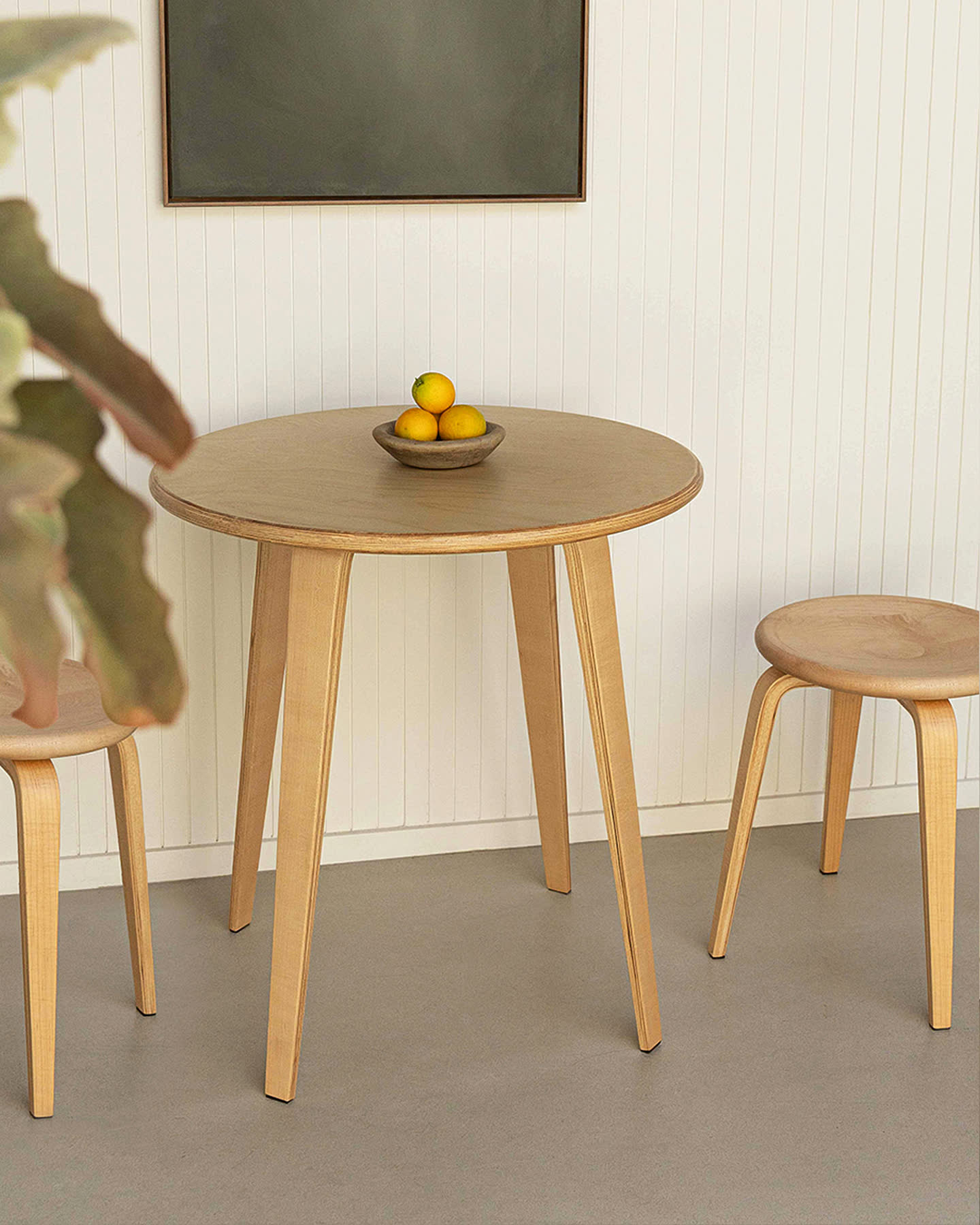The maple Bistro Collection table and stools viewed through a leafy foreground for Sunroom.